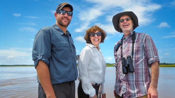 Three people looking at camera in front of river