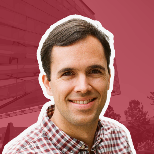 A color photo of a man smiling for a photo with a red background