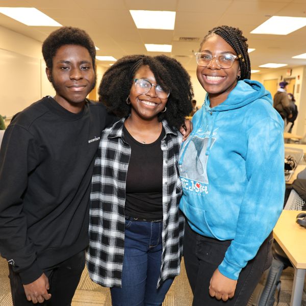 A color photo of a group of 3 people smiling for a photo