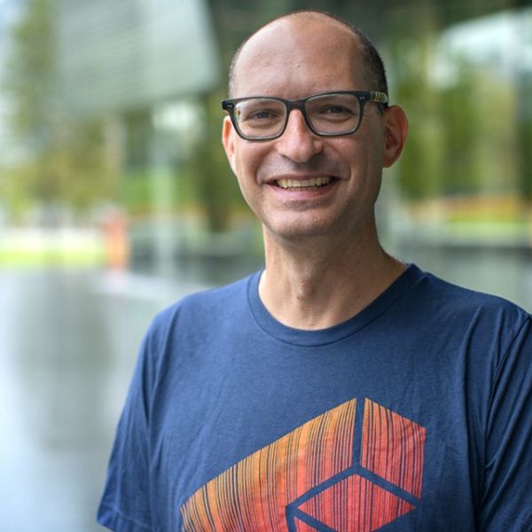 A color photo of a man standing outside, smiling for a photo