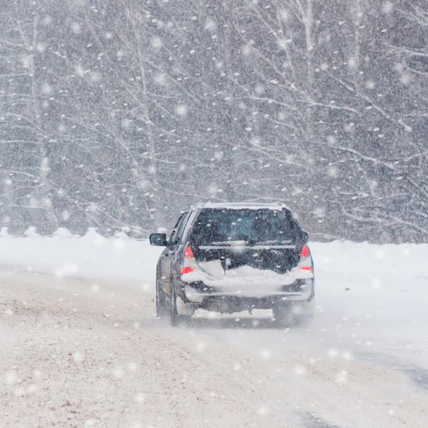 A color photo showing a car driving on a snowy, rural road