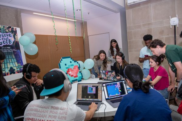 A color photo showing a group of people playing video games on laptop computers while sitting at a large circular table