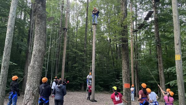 A color photo showing people working together on a ropes course