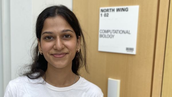 A color photo of a woman standing next to a sign for computational biology, smiling for a photo