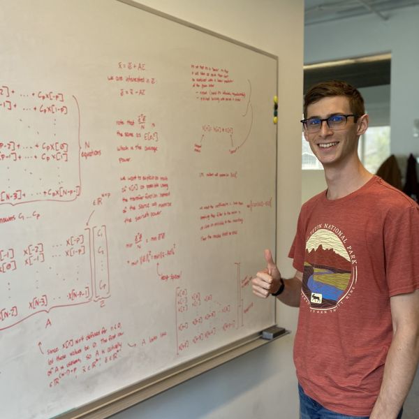 Jason Klein A color photo of a man standing beside a chalkboard with his thumbs up