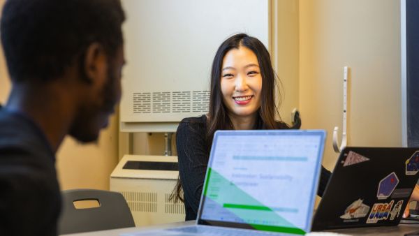 A color photo of a woman talking with a man while seated near a laptop