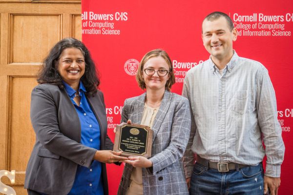 A color photo showing 3 people smiling for a photo, with the woman in the middle holding an award