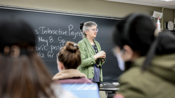 A color photo showing a woman teaching in front of a class