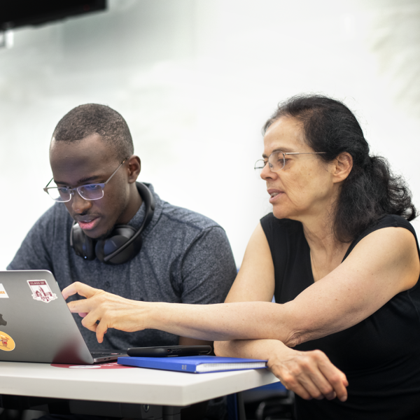 A color photo showing a man and woman working on a laptop computer